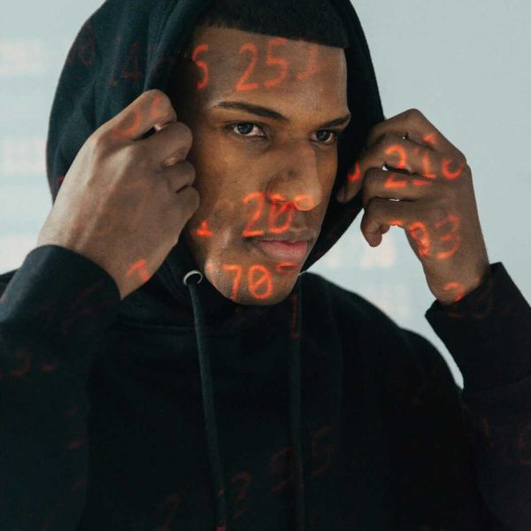 Portrait of a cybersecurity expert wearing a hoodie with projected digital data and numbers.